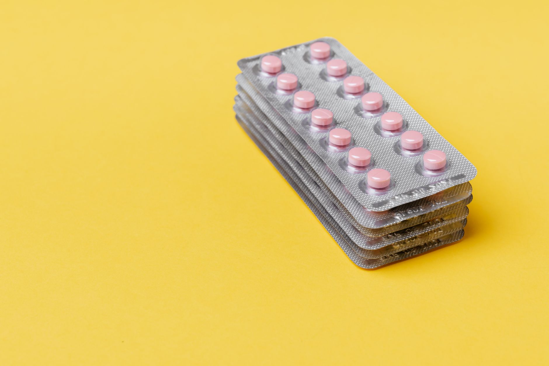 A stack of silver blister packs of small pink tablets on a bright yellow surface.