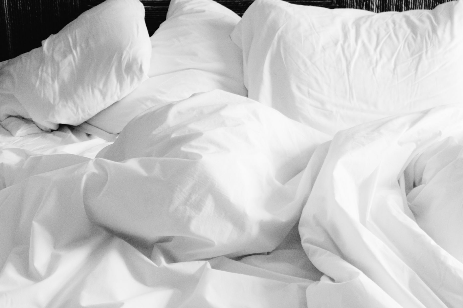 Rumpled white pillows and a white duvet against a dark wooden headboard.
